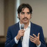 Alvaro talking through a microphone, wearing a blue blazer with a white shirt