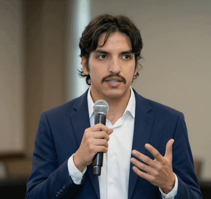 Alvaro talking through a microphone, wearing a blue blazer with a white shirt